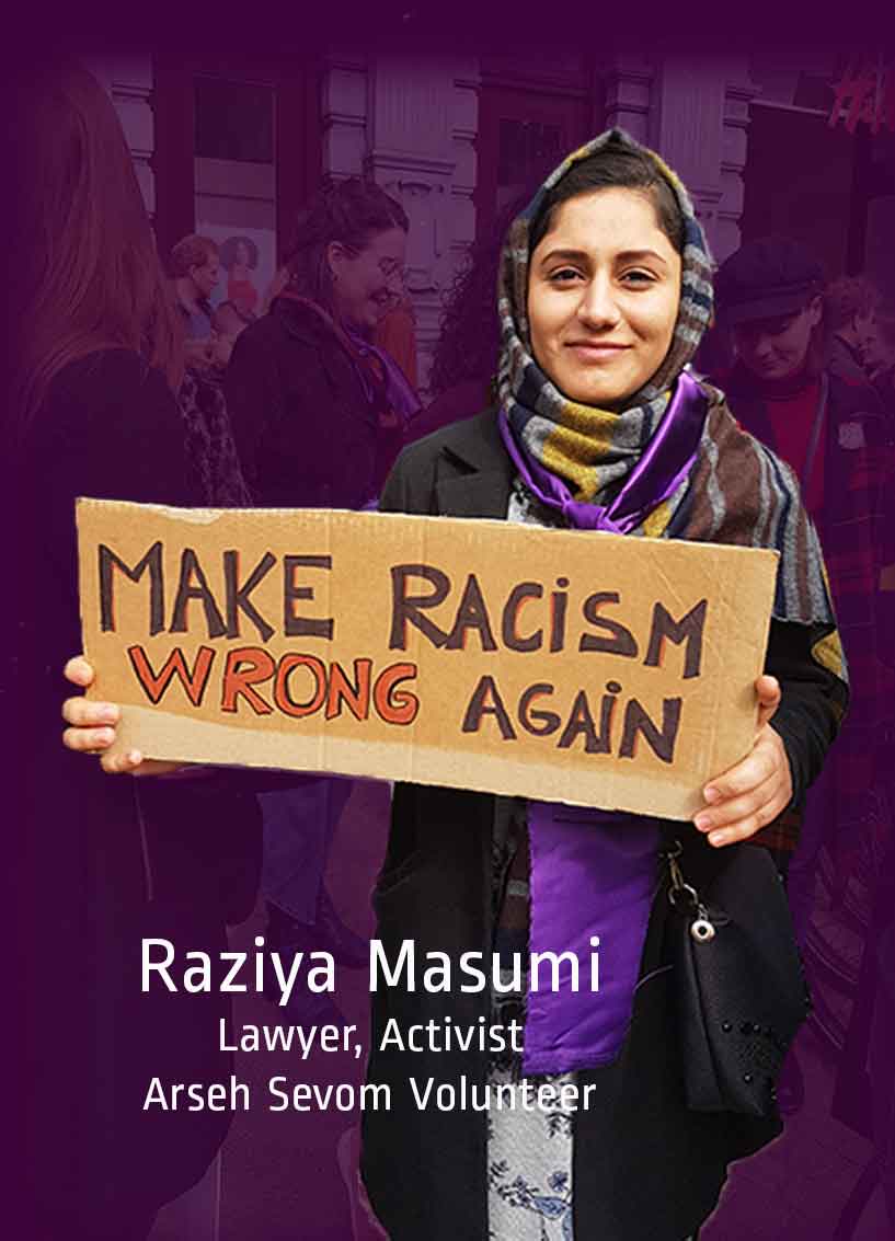 Young woman wearing a multi-colored scarf and holding a cardboard sign that reads "Make Racism Wrong Again"